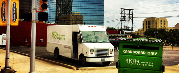 A KB Recycling truck parked downtown Amarillo Texas. In front of the truck is a green cardboard dumpster that KB Recycling uses for their commercial recycling services.